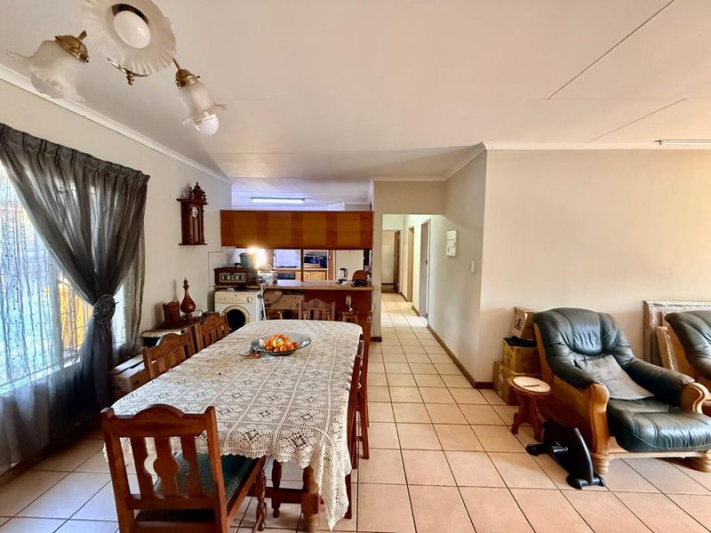 Open-plan dining and kitchen area featuring tiled flooring and dated cabinetry, providing a functional layout with direct access to the home's passageway.