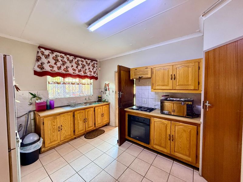 A functional kitchen featuring wooden cabinetry, built-in oven, electric hob, and tiled flooring, offering a classic layout with potential for modern updates.