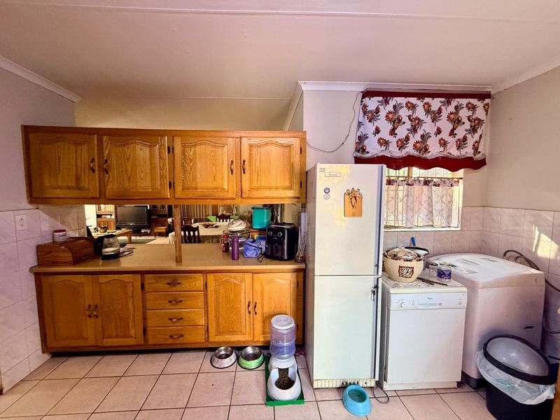 A functional kitchen featuring traditional wooden cabinetry, tiled flooring, and a tiled splashback, offering a practical layout with potential for modern updates.