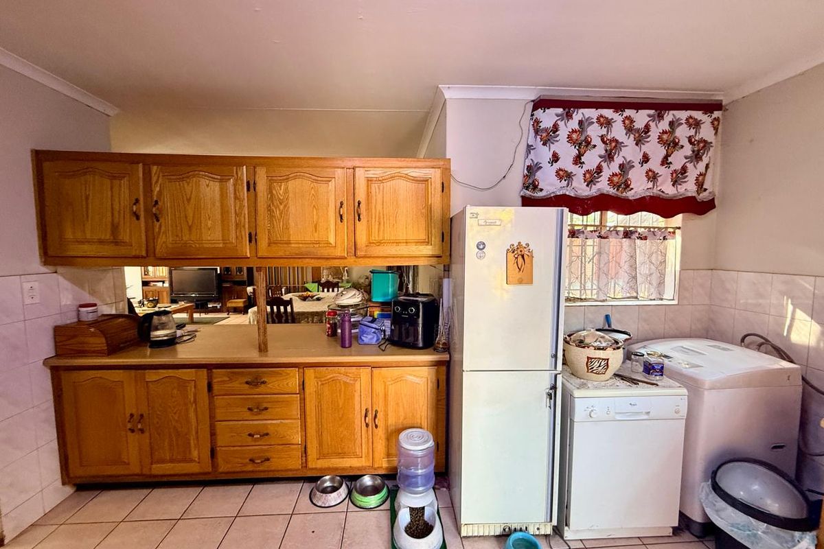 A functional kitchen featuring traditional wooden cabinetry, tiled flooring, and a tiled splashback, offering a practical layout with potential for modern updates.