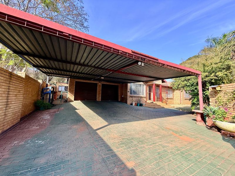 Front exterior view featuring a double garage, a large covered carport, and brick paved driveway with perimeter walling.