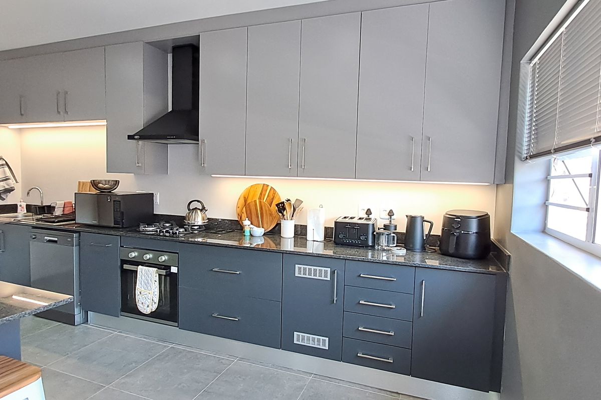 Modern kitchen featuring sleek grey cabinetry, granite countertops, integrated appliances, and under-cabinet lighting, offering a clean and functional culinary space.