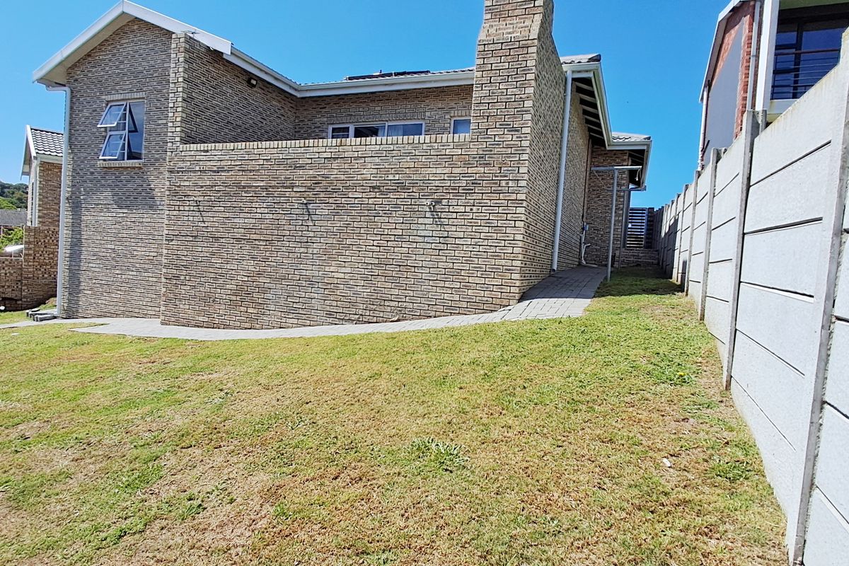 Rear view of the property featuring a face brick facade, paved walkway, and enclosed garden area with precast concrete boundary walls.