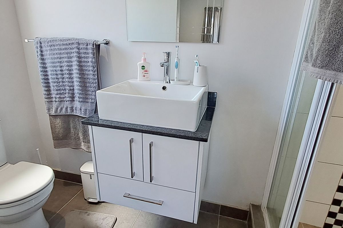 A modern bathroom featuring a white vessel sink on a vanity cabinet, a toilet, and a shower enclosure with tiled flooring.