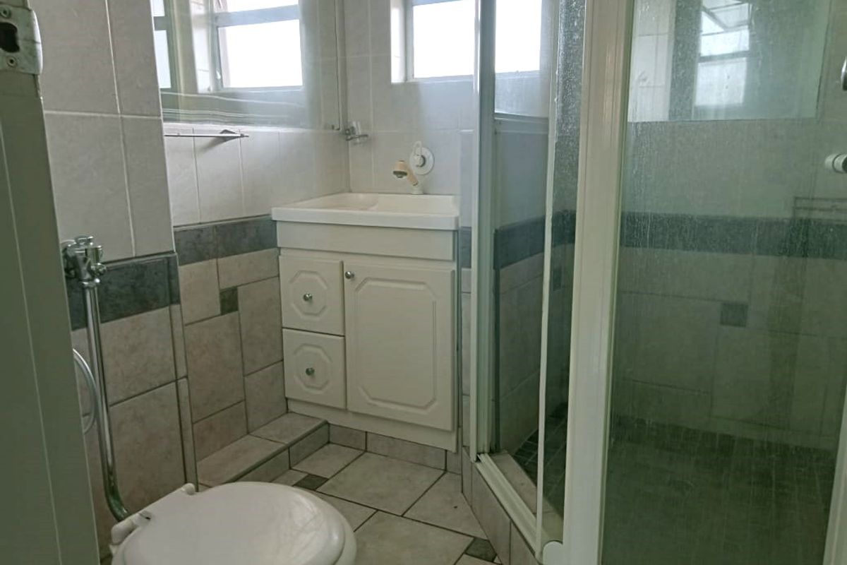 A functional bathroom featuring a tiled shower enclosure, a vanity basin, and a toilet, with neutral wall and floor tiling throughout.