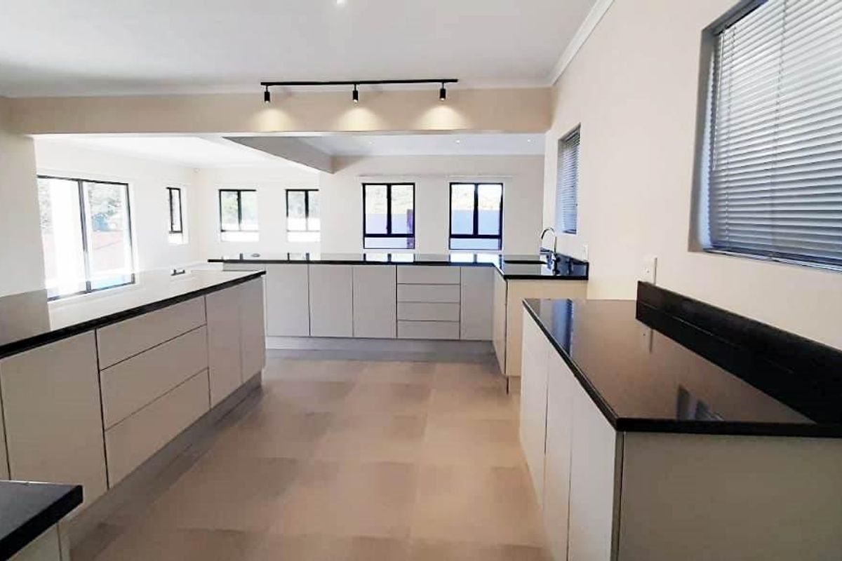 A spacious, modern kitchen featuring extensive built-in cabinetry, dark granite countertops, and track lighting, flowing into an open-plan living area.