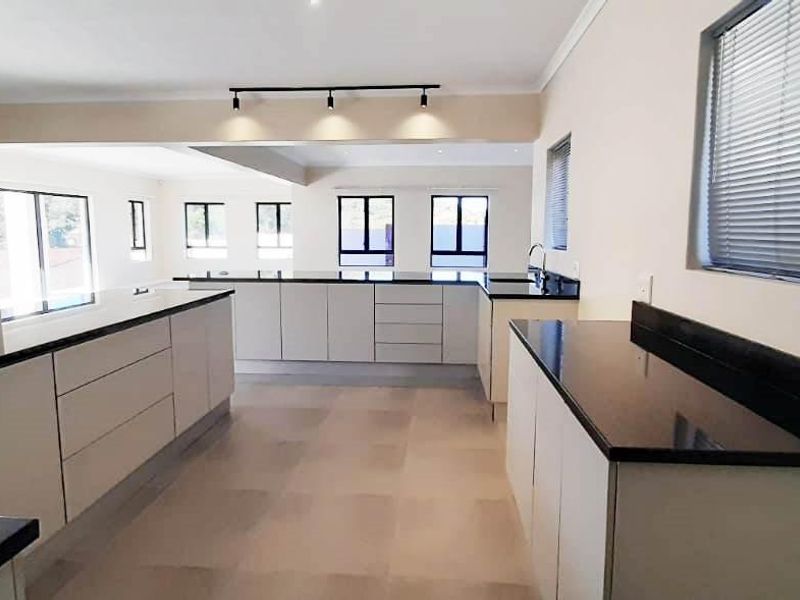 A spacious, modern kitchen featuring extensive built-in cabinetry, dark granite countertops, and track lighting, flowing into an open-plan living area.