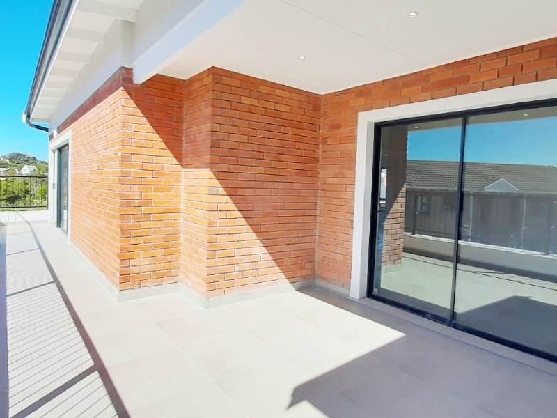 A spacious, modern balcony featuring exposed brickwork, tiled flooring, and large sliding glass doors, offering a clean and well-maintained outdoor living space.