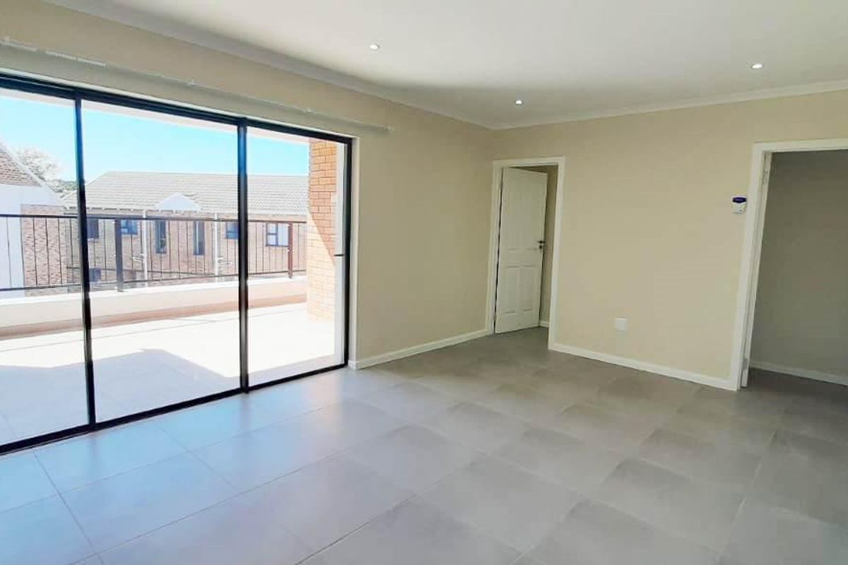 A bright, empty living area featuring large sliding glass doors that open onto a balcony, finished with neutral floor tiles and recessed lighting.