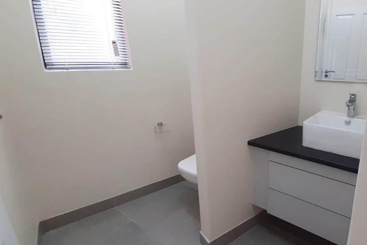 A clean, modern bathroom featuring a vanity with a vessel sink, a wall-mounted toilet, and neutral tiled flooring.