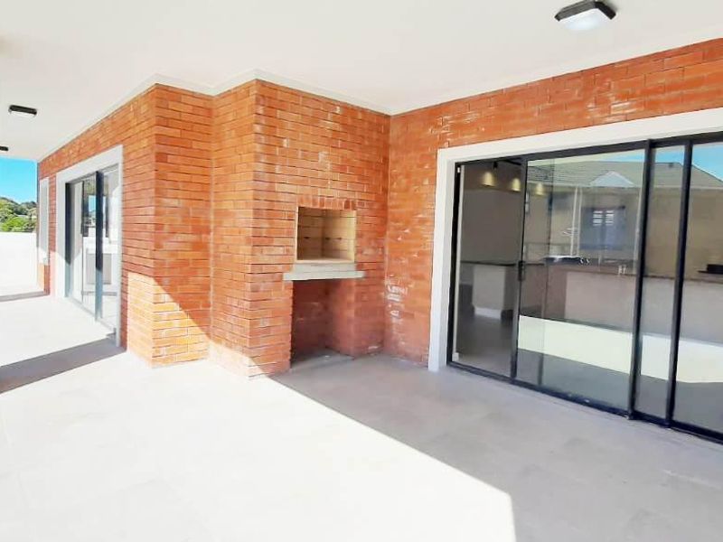 A spacious covered patio featuring exposed brick walls, a built-in braai, and large sliding glass doors providing seamless access to the interior living space.