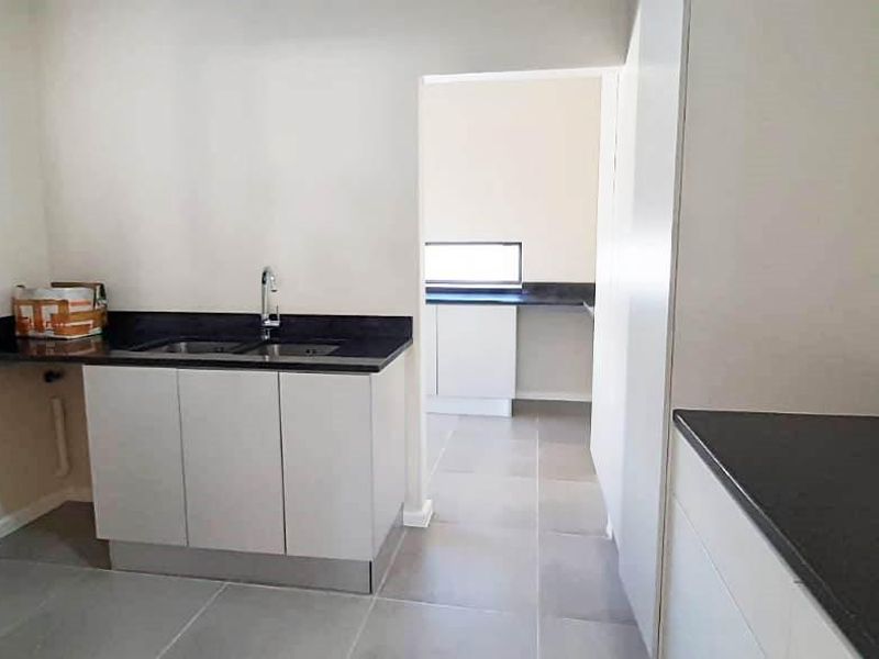 A clean, modern scullery featuring white cabinetry, dark granite countertops, a double sink, and neutral tiled flooring, providing ample workspace and storage.