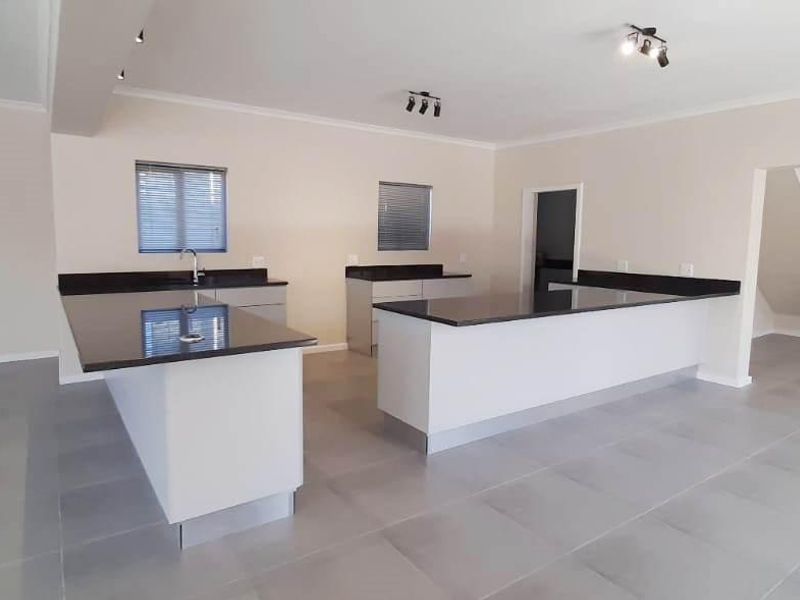 Modern, spacious kitchen featuring sleek granite countertops, ample cabinetry, and neutral tiled flooring, seamlessly integrated into an open-plan living area.