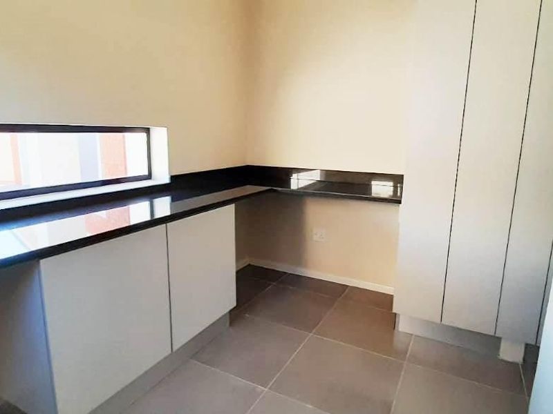 A clean, modern scullery featuring built-in cabinetry, dark granite countertops, and neutral floor tiles, providing ample storage and workspace.