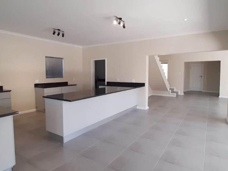 Spacious open-plan kitchen and living area featuring modern granite countertops, a central island, tiled flooring, and large sliding doors leading to the exterior.