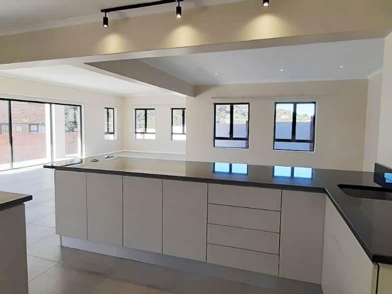 Spacious open-plan kitchen and living area featuring modern cabinetry, granite countertops, sleek track lighting, and large windows providing ample natural light.