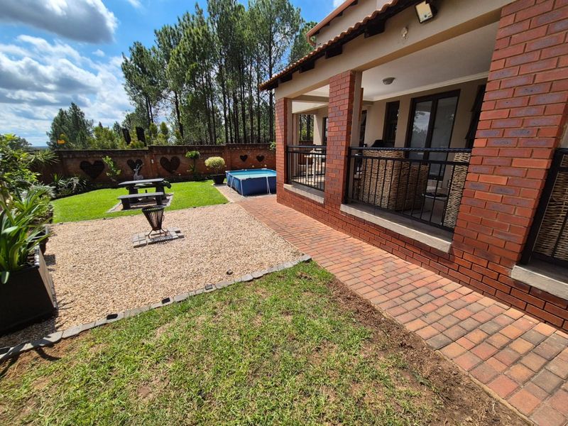 Rear view of the property featuring a covered brick patio, paved walkway, and a landscaped garden with a boundary wall.