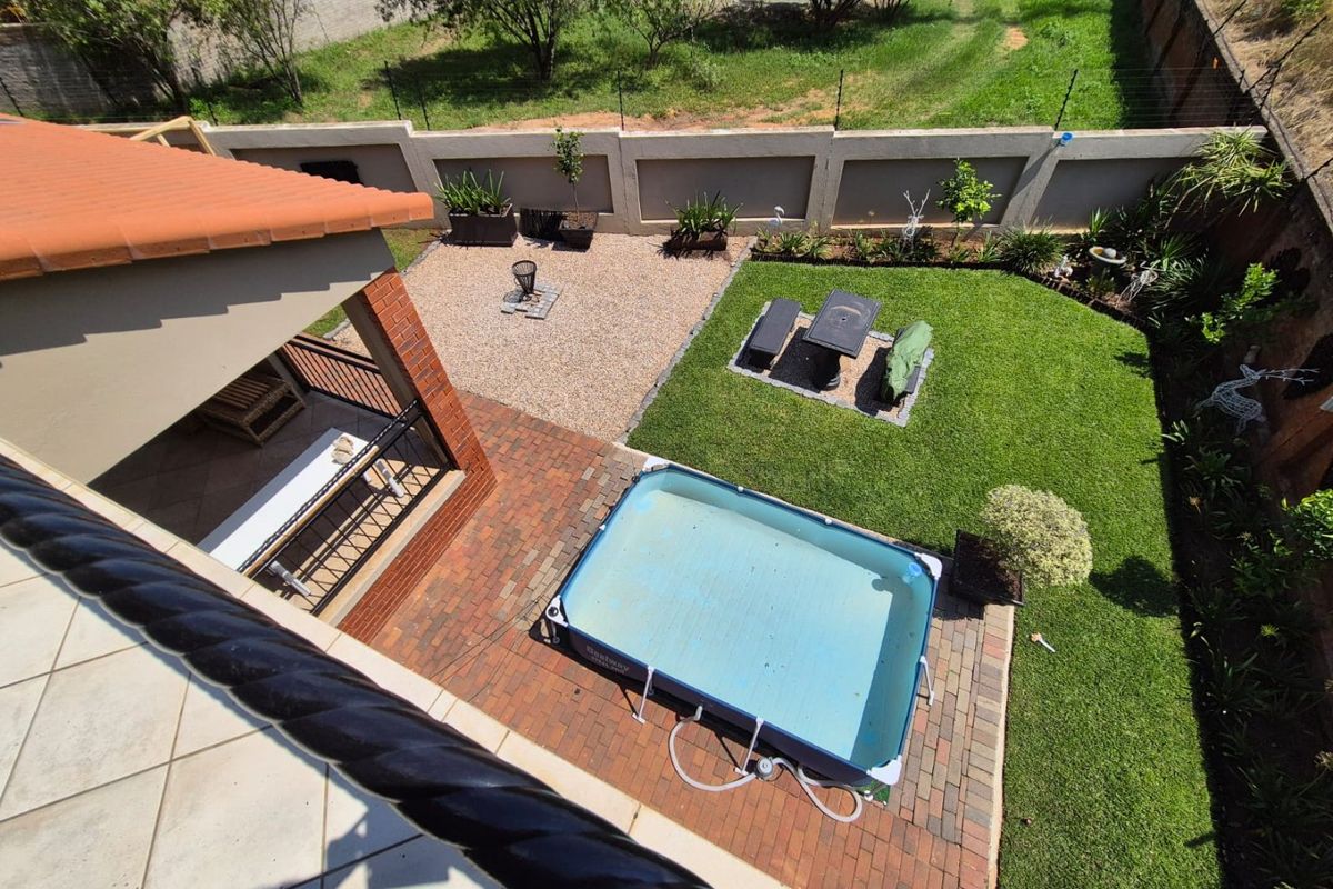 Aerial view of a residential backyard featuring a covered patio, brick-paved area, lawn, and perimeter walling.
