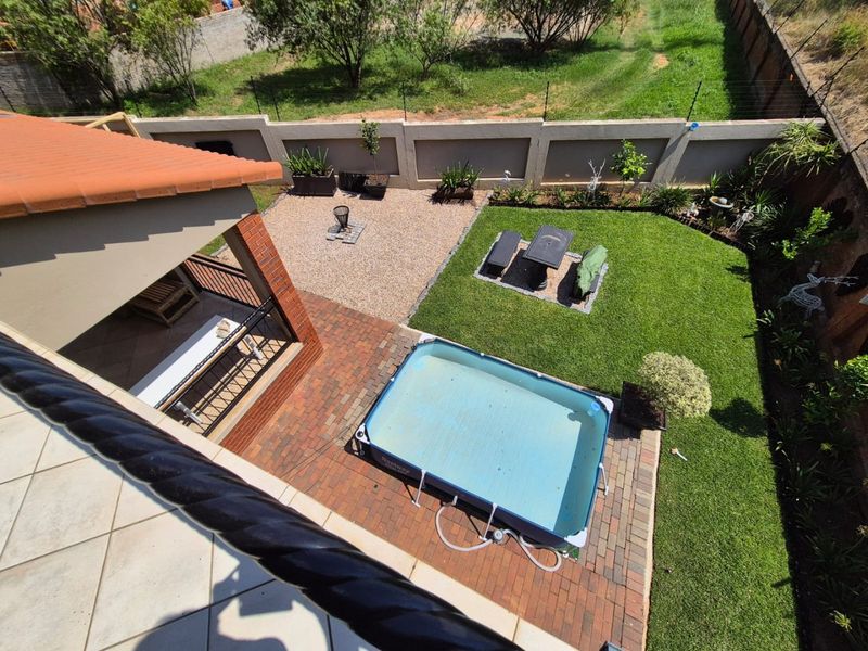 Aerial view of a residential backyard featuring a covered patio, brick-paved area, lawn, and perimeter walling.
