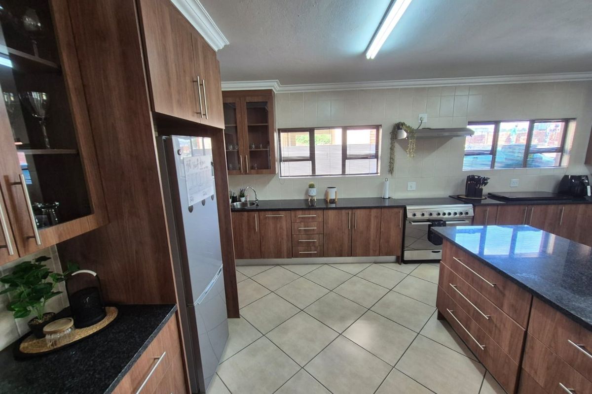 A well-maintained kitchen featuring wood-finish cabinetry, granite countertops, a central island, and tiled flooring with ample natural light.