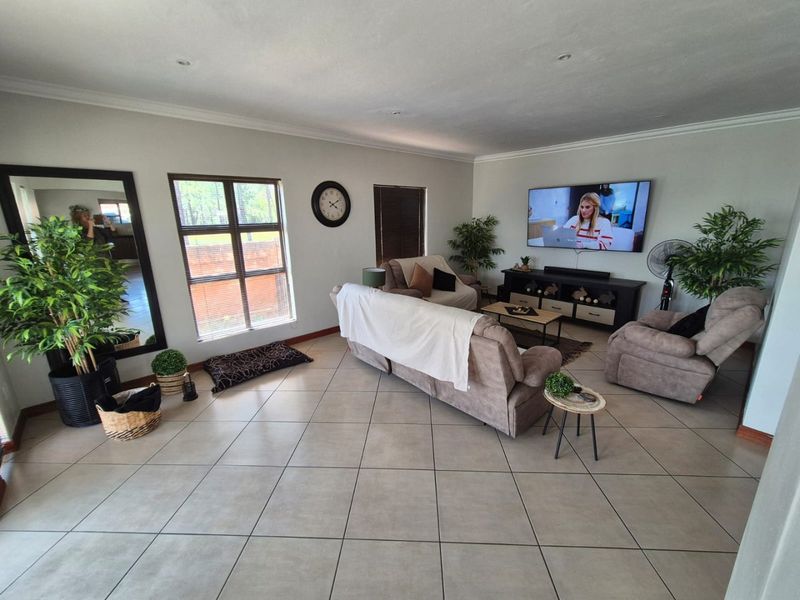 Spacious living room featuring neutral tiled flooring, recessed downlighting, and large windows, providing a bright and comfortable area for relaxation.