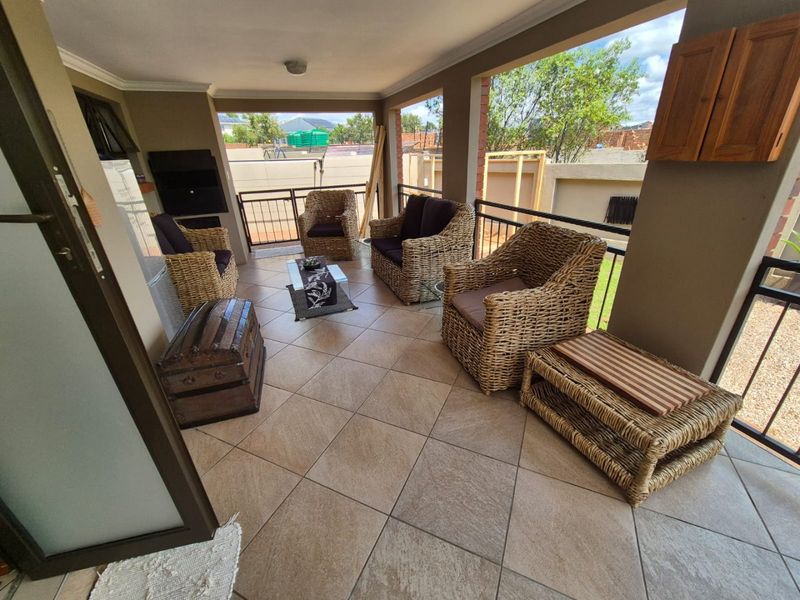 A covered patio area featuring tiled flooring, a built-in braai, and metal balustrades, providing a functional outdoor entertainment space.