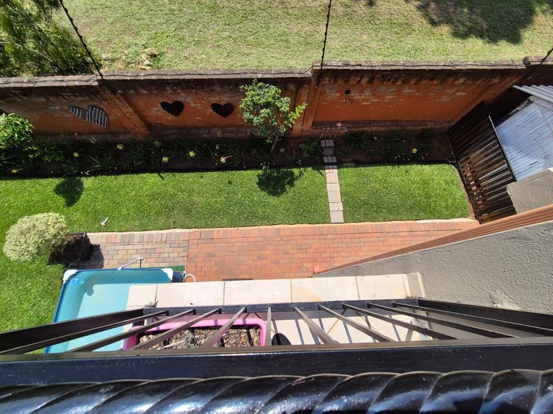 Elevated view of a private rear garden featuring a paved patio, small lawn, plunge pool, and a decorative brick boundary wall.