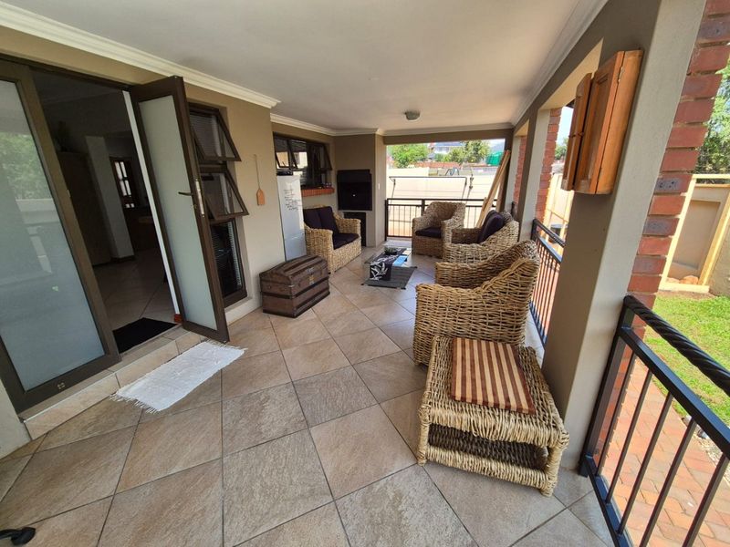 Covered patio area featuring tiled flooring, a built-in braai, and metal balustrades, providing a functional outdoor entertainment space overlooking the garden.