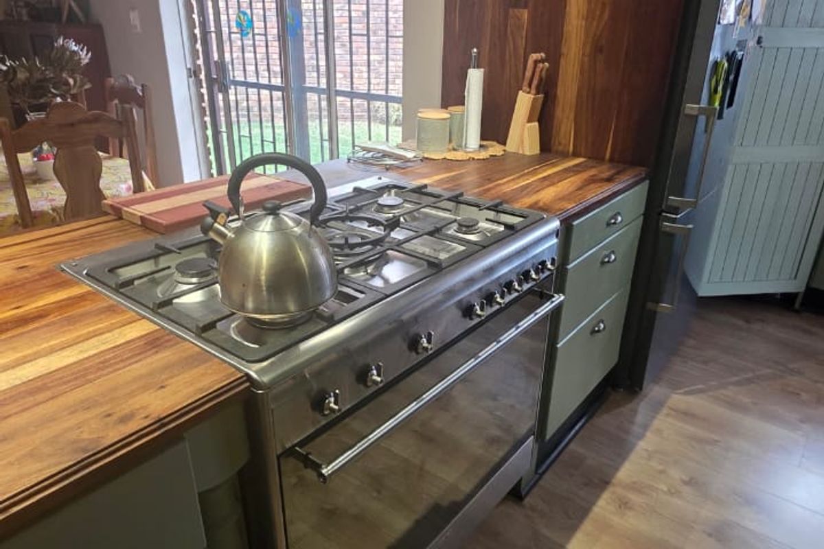 A well-maintained kitchen featuring a gas stove, wooden countertops, and sage green cabinetry, with direct access to the outdoor area via sliding doors.