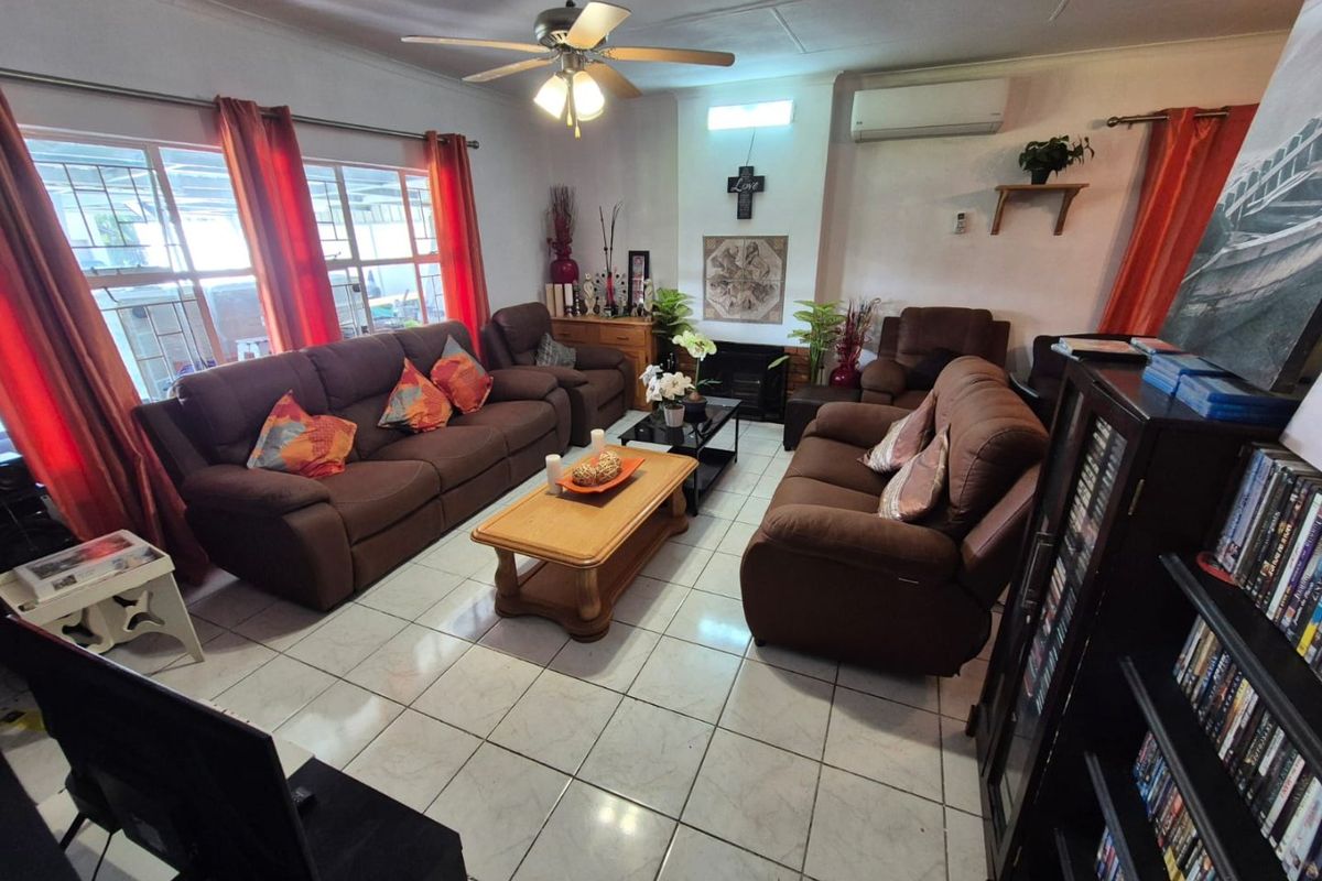 A spacious living room featuring tiled flooring, a ceiling fan, a built-in fireplace, and a wall-mounted air conditioning unit.