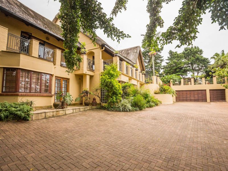 Spacious front exterior view of a large multi-story residence featuring a thatched roof, paved driveway, multiple balconies with iron railings, and a multi-car garage.