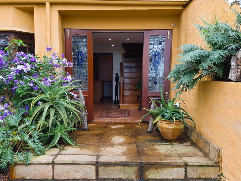A welcoming entrance featuring a stone-paved porch, stained glass double doors, and established garden beds leading into the home.