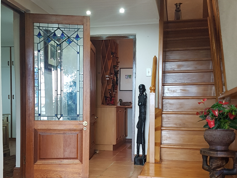 Welcoming entrance hall featuring terracotta floor tiles, a classic stained glass timber door, and a solid timber staircase leading to the upper level.