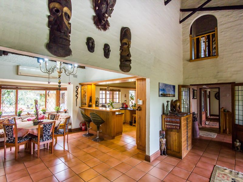 Spacious open-plan living and kitchen area featuring terracotta tiling, exposed timber beams, a breakfast bar, and an internal mezzanine balcony overlooking the space.