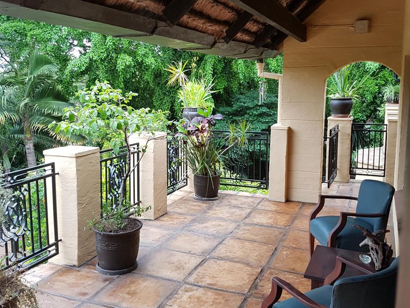 A covered patio featuring a traditional thatched roof, tiled flooring, and decorative wrought iron railings overlooking a lush garden.
