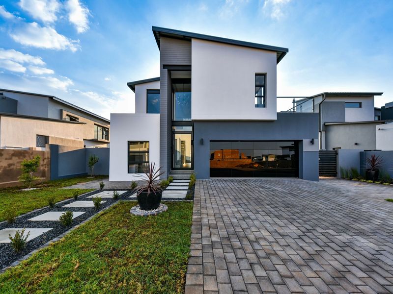 Modern double-story residential home featuring a paved driveway, double garage, and landscaped front garden with a contemporary architectural facade.