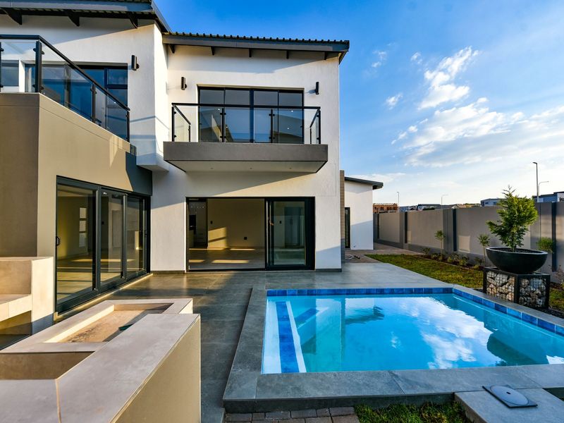 Modern rear exterior featuring a swimming pool, tiled patio area, glass balustrades, and large sliding doors leading into the home.