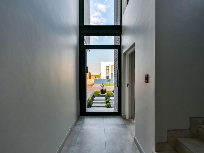 A bright and modern entrance hall featuring large format floor tiles, a full-height glass door, and a staircase leading to the upper level.