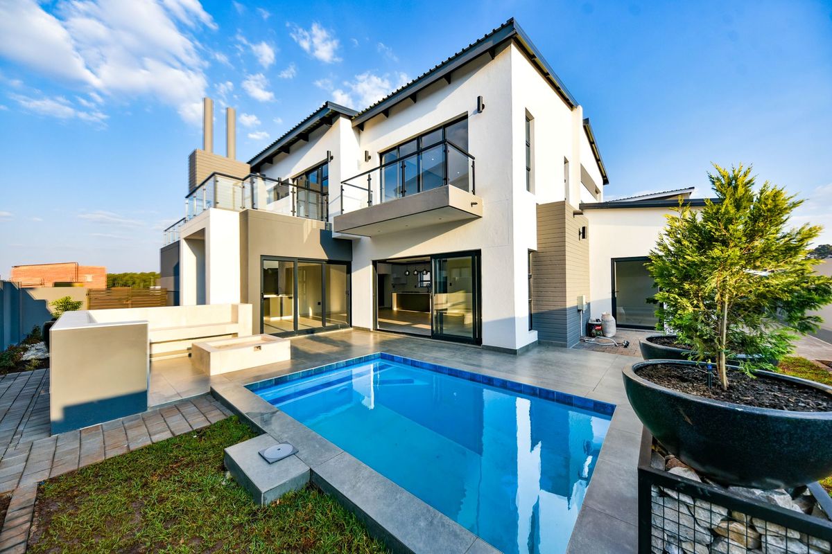 Modern double-story rear elevation featuring a swimming pool, built-in fire pit area, tiled patio, and upper-level balconies with glass balustrades.