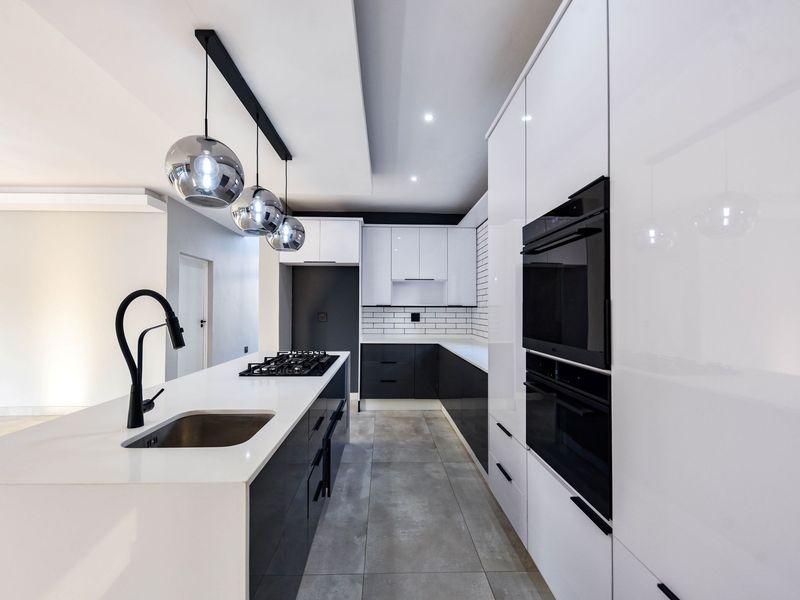 Modern kitchen featuring a central island, high-gloss cabinetry, built-in appliances, subway tile backsplash, and contemporary pendant lighting.