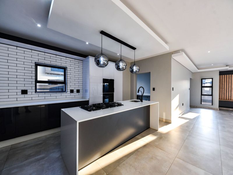 Modern open-plan kitchen featuring a central island with gas cooktop, sleek cabinetry, subway tile backsplash, and high-end finishes in a bright, spacious layout.