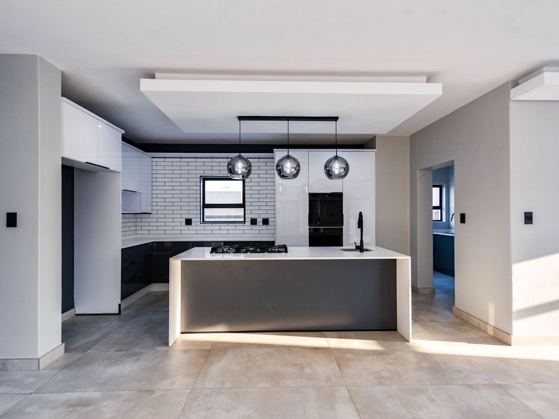 Modern kitchen featuring a central island with gas hob, sleek cabinetry, subway tile backsplash, and contemporary pendant lighting in an open-plan layout.