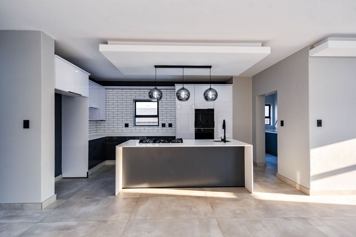 Modern kitchen featuring a central island with gas hob, sleek cabinetry, subway tile backsplash, and contemporary pendant lighting in an open-plan layout.