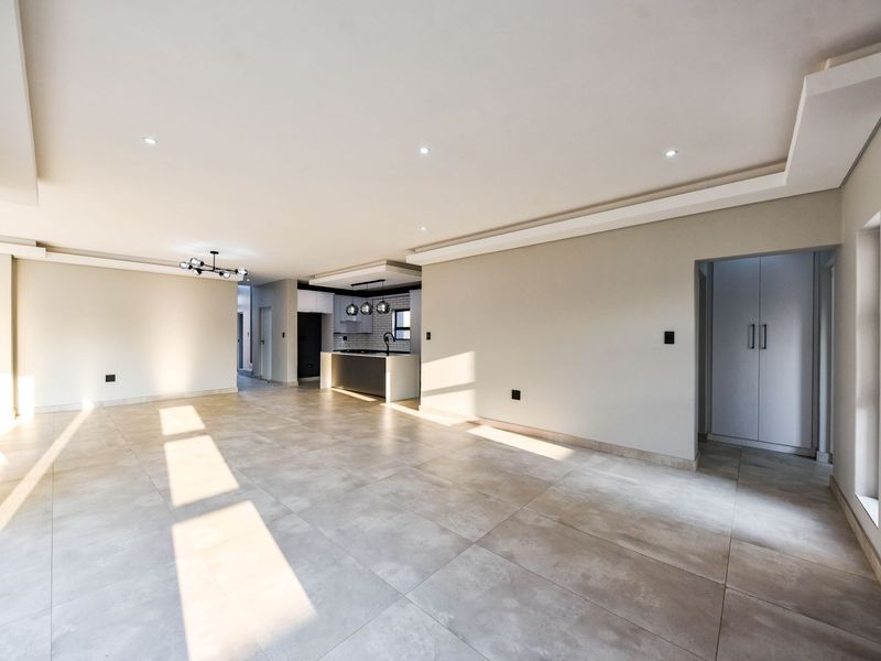 Spacious open-plan living area featuring large format floor tiles, recessed ceiling lighting, and a modern kitchen with a central island and built-in cabinetry.