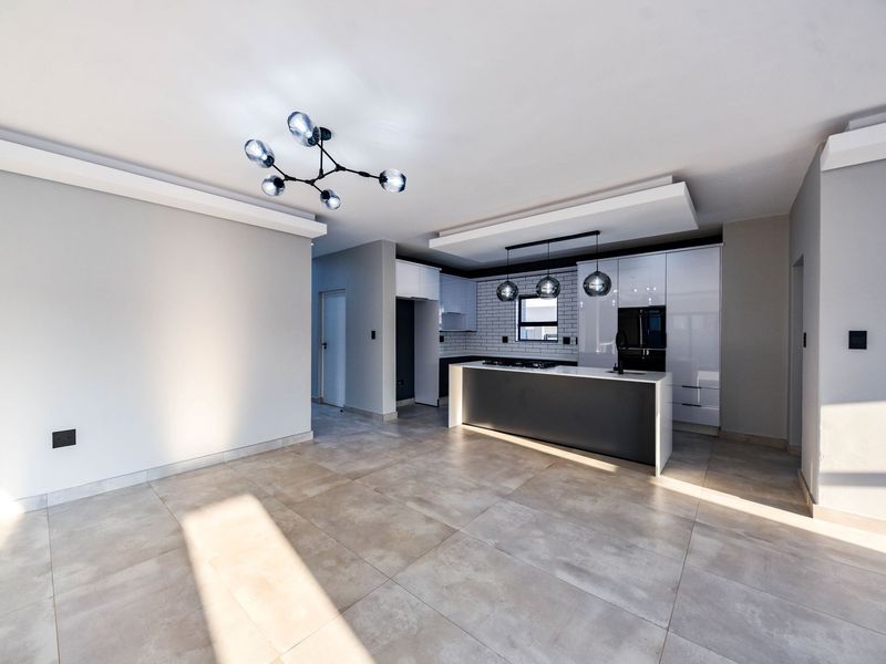 Modern open-plan kitchen and living area featuring a sleek island, built-in appliances, subway tile backsplash, and contemporary lighting fixtures.
