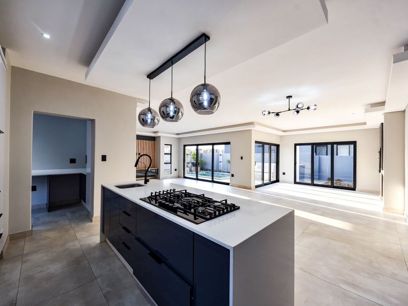Spacious open-plan kitchen and living area featuring a modern island with gas hob, sleek cabinetry, and large sliding doors opening to the pool area.