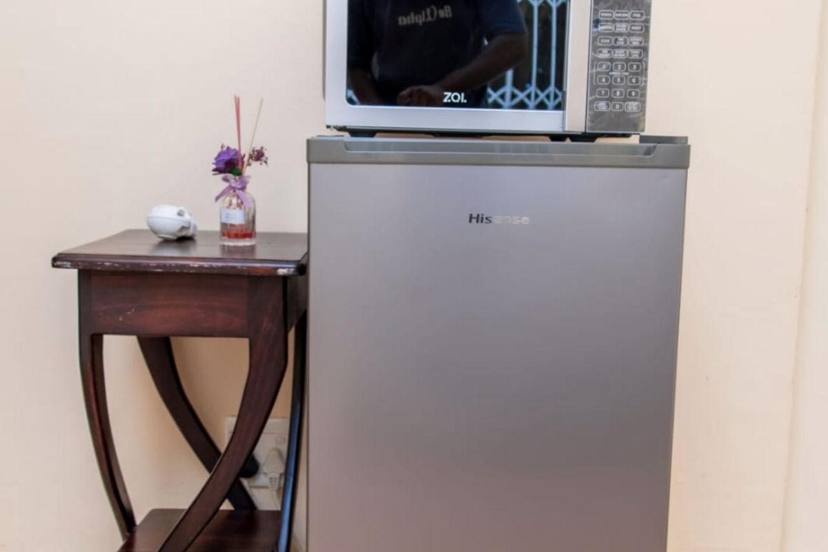 A small kitchenette or refreshment station featuring a compact refrigerator and microwave, set against a plain wall with tiled flooring.