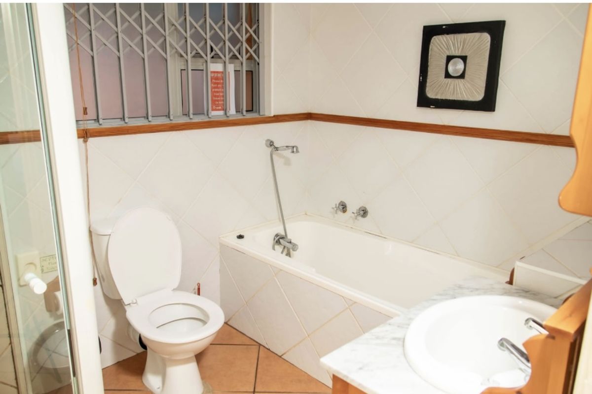 A functional bathroom featuring a built-in bathtub, a pedestal toilet, and a vanity with a marble countertop and integrated sink.