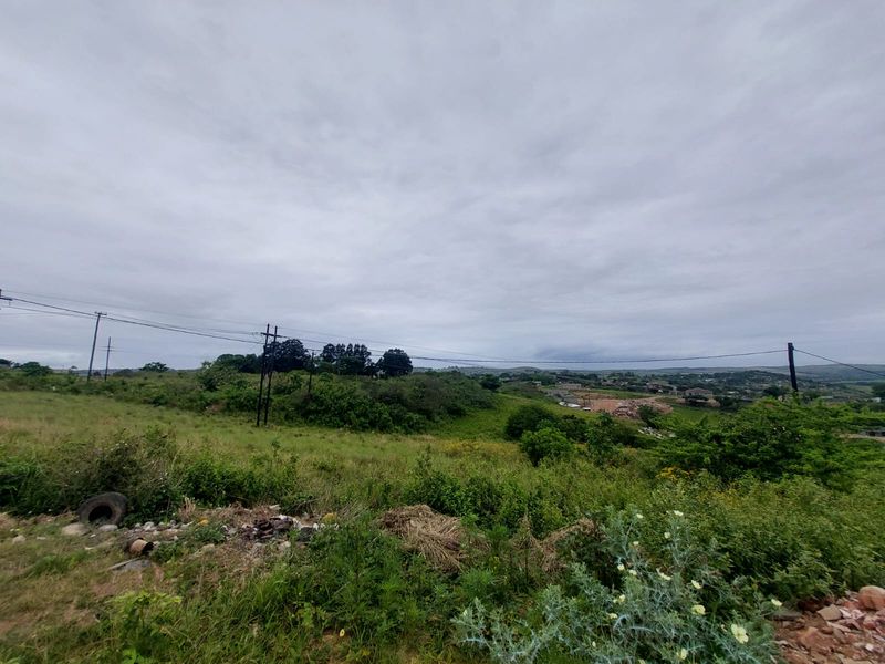 A wide-angle view of a vacant residential plot featuring natural vegetation, rolling landscape, and visible overhead utility infrastructure.