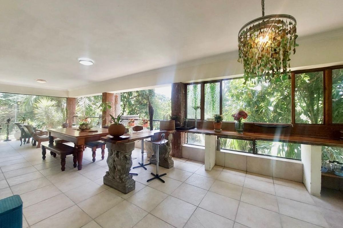 Spacious covered patio featuring tiled flooring, stone pillars, and a built-in wooden counter, offering a bright and airy space with large windows.